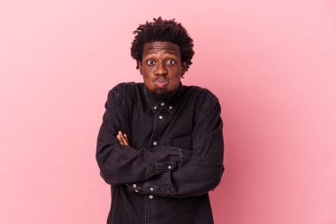 Pembe arka planda izole edilmiş genç Afrikalı Amerikalı adam yanaklarına üflüyor, yorgun bir ifade takınıyor. Yüz ifadesi kavramı.