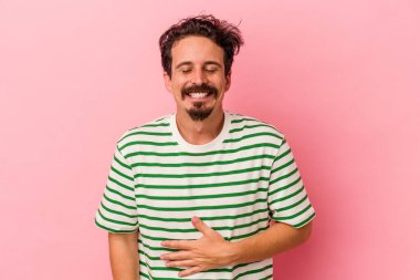 Pembe arka planda izole edilmiş genç beyaz adam karnına dokunuyor, nazikçe gülümsüyor, yemek yiyor ve tatmin oluyor..