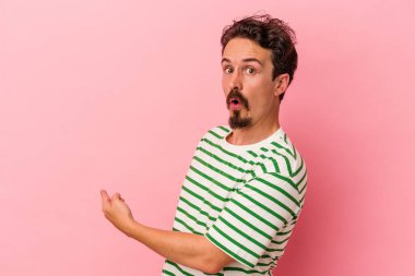 Pembe arka planda izole edilmiş genç beyaz adam gülümsüyor ve boş alanda bir şeyler gösteriyor..