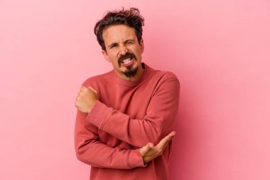 Genç beyaz adam pembe arka planda izole edilmiş dirsek masajı yapıyor, kötü bir hareketin ardından acı çekiyor..