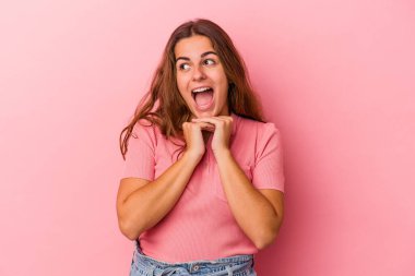 Pembe arka planda izole edilmiş genç beyaz bir kadın şans için dua ediyor, hayrete düşüyor ve ağzını açıp önüne bakıyor..