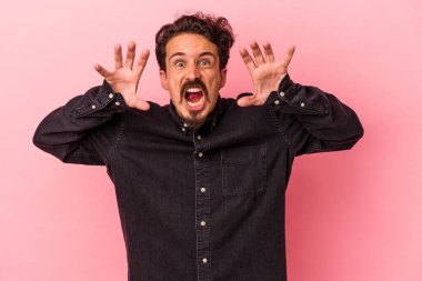 Pembe arka planda izole edilmiş genç beyaz adam pençelerini kedi taklidi yaparken gösteriyor, agresif bir hareket..