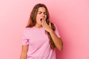 Pembe arka planda izole edilmiş genç beyaz kadın esniyor. Ağzı eliyle kapatan yorgun bir hareket sergiliyor..