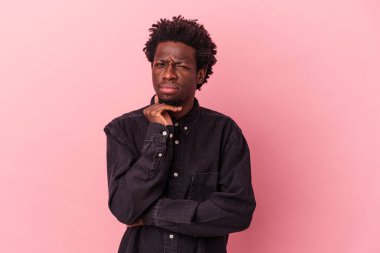 Genç Afrikalı Amerikalı adam pembe arka planda izole edilmiş şüpheli, belirsiz, seni muayene ediyor..