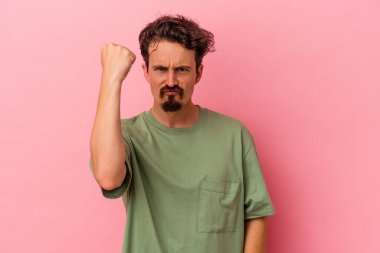 Pembe arka planda izole edilmiş genç beyaz adam yumruğunu kameraya gösteriyor, agresif yüz ifadesi var..