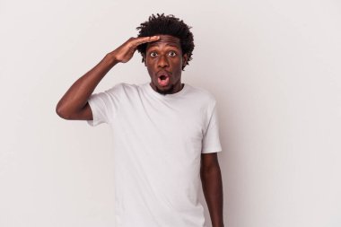 Genç Afrikalı Amerikalı adam beyaz arka planda izole edilmiş, uzaklara bakıyor ve elini alnına koyuyor..