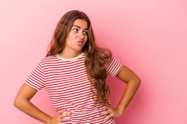 Pembe arka planda izole edilmiş genç beyaz kadın kafası karışmış, kuşkulu ve güvensiz hissediyor..