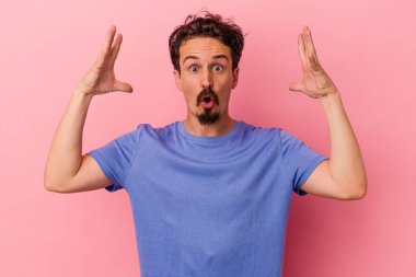 Pembe arka planda izole edilmiş genç beyaz bir adam zaferi ya da başarıyı kutluyor, şaşırıyor ve şok oluyor..