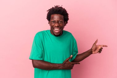 Pembe arka planda izole edilmiş genç Afro-Amerikalı adam işaret parmağıyla işaret ederek heyecanlanıyor..