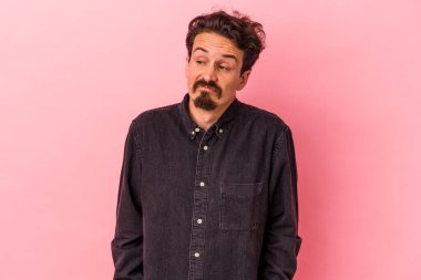 Pembe arka planda izole edilmiş genç beyaz adam omuzlarını silkeliyor ve gözleri açık..