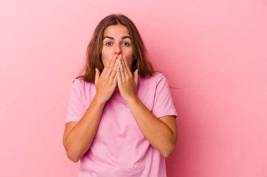 Pembe arka planda izole edilmiş genç beyaz kadın şok olmuş, ağzı ellerle kaplanmış, yeni bir şey keşfetmeye hevesli..
