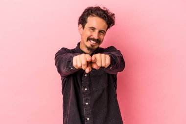 Pembe arka planda izole edilmiş genç beyaz adam parmaklarıyla ön tarafı işaret ediyor..