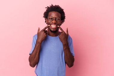 Genç Afro-Amerikalı adam pembe arka planda izole edilmiş gülümsüyor, parmaklarını ağıza doğrultuyor..