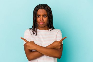 Genç Afrikalı Amerikalı kadın mavi arka planda iki seçenek arasından seçim yapmaya çalışıyor..