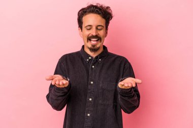 Pembe arka planda izole edilmiş genç beyaz bir adam elinde avuç içi bir şeyle kameraya sunuyor..