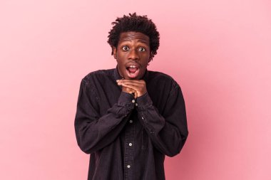 Genç Afrikalı Amerikalı bir adam pembe arka planda izole edilmiş şans için dua ediyor, hayrete düşüyor ve ağzını açıyor..