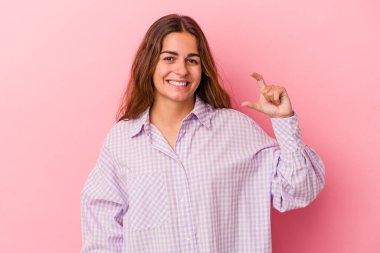 Pembe arka planda izole edilmiş genç beyaz bir kadın işaret parmaklarıyla küçük bir şey tutuyor, gülümsüyor ve kendinden emin..