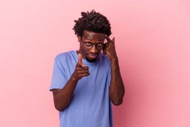 Genç Afrikalı Amerikalı bir adam pembe arka planda izole edilmiş. Parmağıyla tapınağı işaret ediyor, düşünüyor ve bir göreve odaklanıyor..