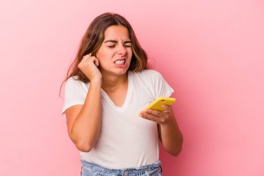 Pembe arka planda izole edilmiş cep telefonu kullanan beyaz bir kadın kulaklarını elleriyle kapatıyor..