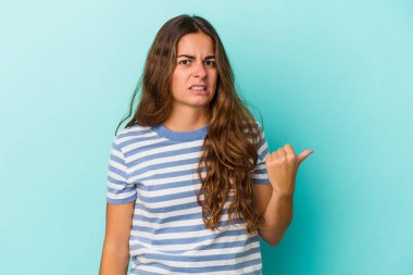 Mavi arka planda izole edilmiş genç beyaz kadın işaret parmağıyla fotokopi alanını işaret ederek şok oldu..