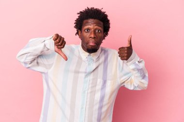 Genç Afro-Amerikalı, pembe arka planda izole edilmiş, baş parmağını kaldırıyor, zor bir seçim.