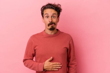Pembe arka planda izole edilmiş genç beyaz adam karnına dokunuyor, nazikçe gülümsüyor, yemek yiyor ve tatmin oluyor..