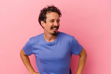 Pembe arka planda izole edilmiş genç beyaz adam mutlu bir şekilde gülüyor ve ellerini karnının üstünde tutarak eğleniyor..