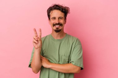 Pembe arka planda izole edilmiş genç beyaz adam iki numarayı parmaklarıyla gösteriyor..