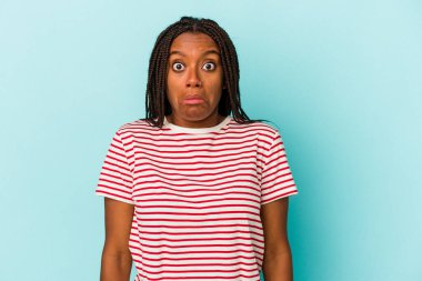 Young african american woman isolated on blue background  shrugs shoulders and open eyes confused. clipart
