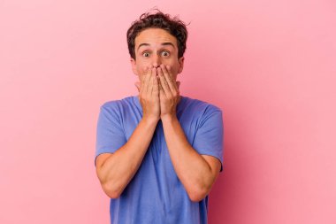 Pembe arka planda izole edilmiş genç beyaz adam elleriyle ağzını kapatırken şok oldu..
