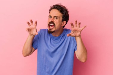 Pembe arka planda izole edilmiş genç beyaz adam gergin elleriyle çığlık atıyor..