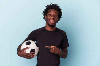 Amerikan futbolu oynayan genç Afro-Amerikalı adam mavi arka planda izole edilmiş gülümsüyor ve boş alanda bir şeyler gösteriyor..