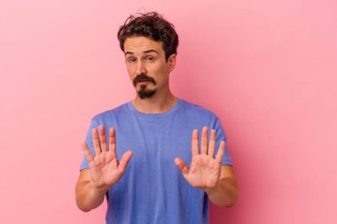 Pembe arka planda izole edilmiş genç beyaz bir adam tiksinti belirtisi gösteren birini reddediyor..
