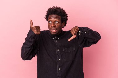Genç Afro-Amerikalı, pembe arka planda izole edilmiş, baş parmağını kaldırıyor, zor bir seçim.