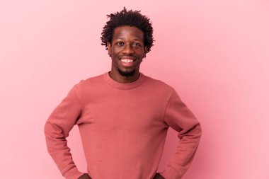 Genç Afrikalı Amerikalı, pembe arka planda izole edilmiş, kendine güveni tam, elleri kalçasında..