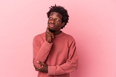 Genç Afro-Amerikalı bir adam pembe arka planda izole edilmiş, bir strateji planlıyor, bir iş hayatının nasıl olacağını düşünüyor..