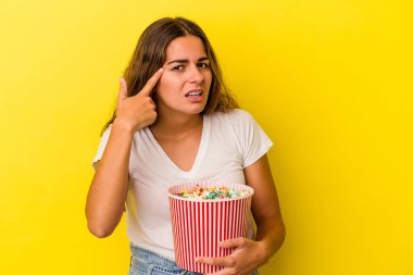 Sarı arka planda izole edilmiş patlamış mısır tutan beyaz bir kadın işaret parmağıyla yaptığı hayal kırıklığını gösteriyor..