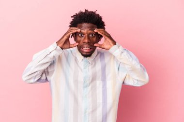 Pembe arka planda izole edilmiş genç Afro-Amerikan bir başarı fırsatı bulmak için gözlerini açık tutuyor..
