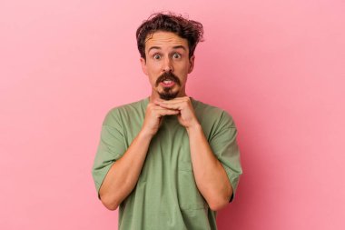 Pembe arka planda izole edilmiş genç beyaz adam şans için dua ediyor, hayrete düşüyor ve ağzını açıp önüne bakıyor..