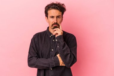 Kafkasyalı genç adam pembe arka planda izole edilmiş düşünüyor ve yukarı bakıyor, yansıtıyor, düşünüyor, bir fantezi kuruyor..