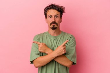 Pembe arka plan noktalarında izole edilmiş genç beyaz adam iki seçenek arasında seçim yapmaya çalışıyor..