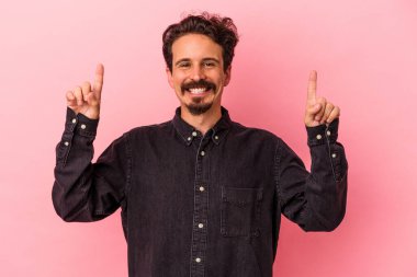 Pembe arka planda izole edilmiş genç beyaz adam iki parmağı da boş bir alan gösteriyor..