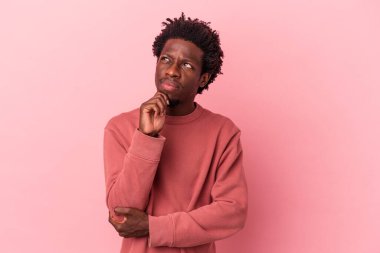 Genç Afrikalı Amerikalı bir adam pembe arka planda izole edilmiş düşünüyor ve yukarı bakıyor, yansıtıyor, düşünüyor, hayal kuruyor..