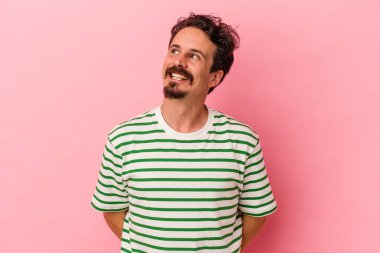 Genç beyaz adam pembe arka planda izole edilmiş rahat ve mutlu bir şekilde gülüyor, boynunda dişlerini gösteriyor..
