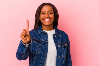 Pembe arka planda izole edilmiş genç Afro-Amerikalı kadın bir numarayı parmağıyla gösteriyor..