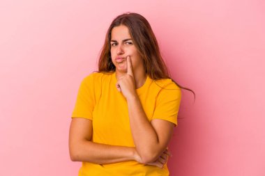 Pembe arka planda izole edilmiş genç beyaz kadın alaycı bir ifadeyle kameraya bakıyor..