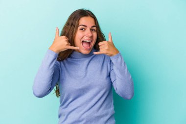 Mavi arka planda izole edilmiş genç beyaz kadın parmaklarıyla bir cep telefonu hareketi gösteriyor..