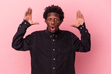 Genç Afrikalı Amerikalı bir adam pembe arka planda izole edilmiş zaferi ya da başarıyı kutluyor, şaşırmış ve şok olmuş..