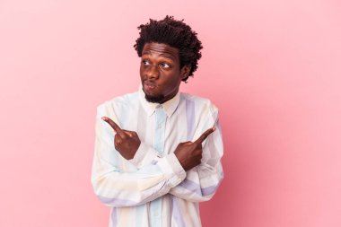 Genç Afrikalı Amerikalı adam pembe arka planda iki seçenek arasında seçim yapmaya çalışıyor..