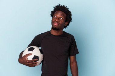 Amerikan futbolu oynayan genç Afro-Amerikalı adam mavi arka planda izole bir şekilde hedeflerine ve amaçlarına ulaşmayı hayal ediyor.